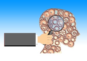 hand holding magnifying glass over brain, which is made up of gears